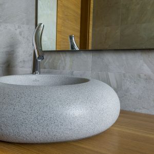 Elegant stone bathroom sink with modern chrome faucet and large mirror.